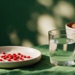 Small red B12 tablets in a ceramic dish with a glass of water and brown eggs on green linen