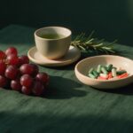 Red grapes, green tea and a dish of capsules on green linen with rosemary