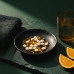 Best Multivitamin for Men: Top 7 Picks Reviewed (2026) Multivitamin capsules in a black ceramic dish with a towel, water and sliced orange on dark slate