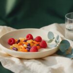 Multivitamin capsules in a pale dish with raspberries, eucalyptus and a glass of water on cream linen