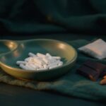 Magnesium capsules in a green ceramic dish with dark chocolate and almonds on forest-green linen