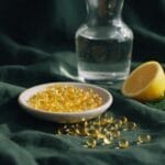 Golden omega-3 softgels in a ceramic dish beside a lemon half and dill on green linen