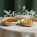 Vitamin D3 vs D3+K2: Do You Really Need K2? (2026 Science Review) Two dishes of softgels side by side in sunlight on a cream linen table with eucalyptus