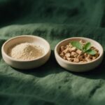 KSM-66 vs Sensoril: Which Ashwagandha Extract Should You Take? Two ceramic dishes with ashwagandha root powder and chopped dried roots with green leaves on green linen