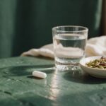 Why Your Magnesium Isn't Working (and How to Fix It) A single white capsule next to a glass of water and a dish of pumpkin seeds and dark chocolate on green stone